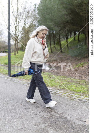 Senior woman walking in park after rain holding closed umbrella Senior woman walking in park after rain holding closed umbrella 130405169