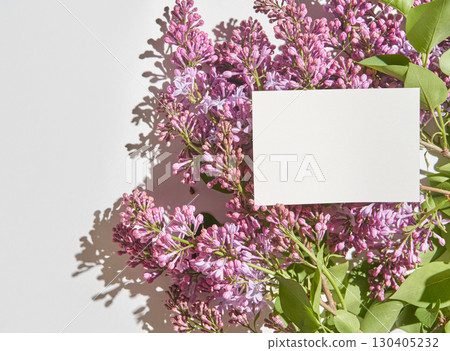 Blank card on lilac flowers arrangement with sunlight shadows on white 130405232