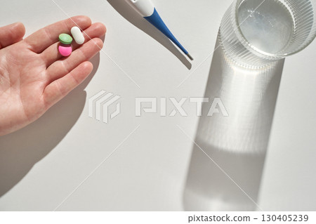 Caucasian adult hand holding pills with thermometer and glass of water on white Caucasian adult hand holding pills with thermometer and glass of water on white 130405239