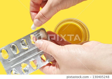 Hands taking pill from blister pack with honey jar on yellow background Hands taking pill from blister pack with honey jar on yellow background 130405248
