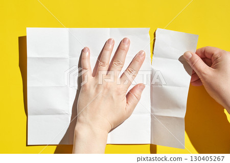 Caucasian female hands tearing white paper on bright yellow background 130405267