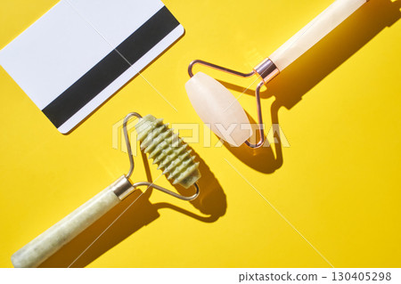 Dual jade and rose quartz facial rollers on vibrant yellow background Dual jade and rose quartz facial rollers on vibrant yellow background 130405298