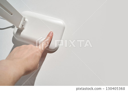 Female hand touching minimalist white desk lamp on clean surface with wired Female hand touching minimalist white desk lamp on clean surface with wired 130405368