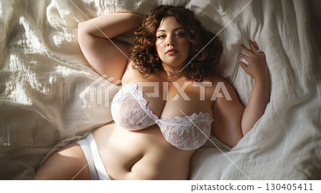 Plus-size woman in lacy underwear lying on bed, embracing her beauty. 130405411