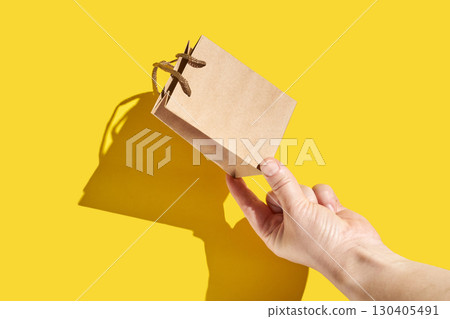 Caucasian adult hand holding small brown paper bag against bright yellow Caucasian adult hand holding small brown paper bag against bright yellow 130405491
