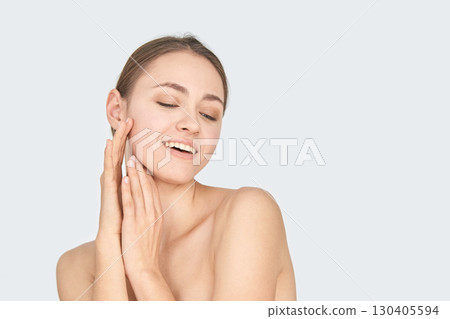 Young caucasian female smiling with eyes closed and hands on face against light 130405594