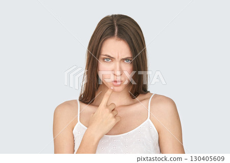 Caucasian young female pondering with finger on chin in thoughtful pose on gray 130405609