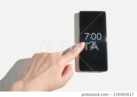 Adult caucasian hand setting alarm clock on smartphone device against white Adult caucasian hand setting alarm clock on smartphone device against white 130405617