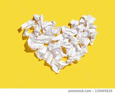 Crumpled white paper sheets shaped into heart on vibrant yellow background 130405629