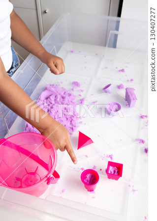 Child playing with purple kinetic sand and pink toy tools 130407277