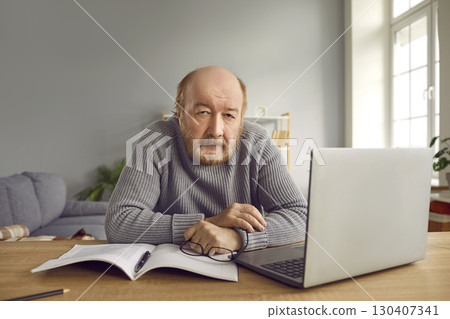 Portrait of senior man sitting with laptop computer at home and looking at the camera. Portrait of senior man sitting with laptop computer at home and looking at the camera. 130407341