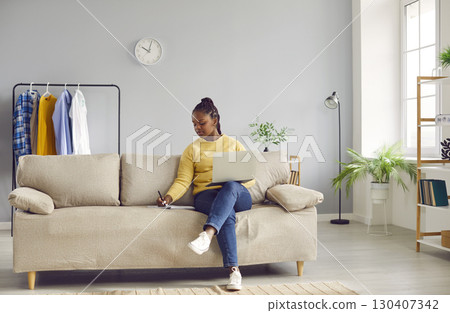 Young african american business woman working with laptop computer at home sitting on sofa. Young african american business woman working with laptop computer at home sitting on sofa. 130407342