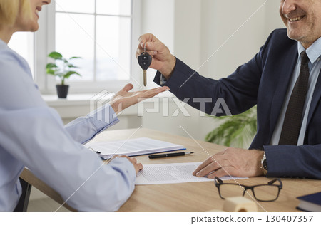 Smiling man real estate agent hands over the key to a happy young woman house owner 130407357