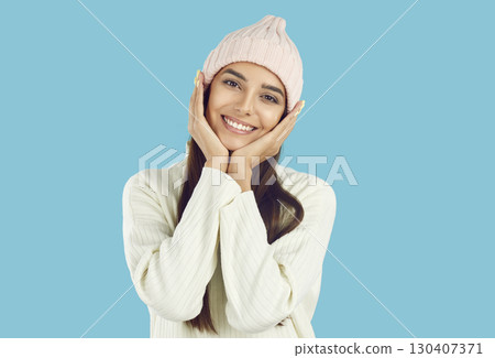 Portrait of beautiful young woman who holds her hands near her cheeks on light blue background. 130407371