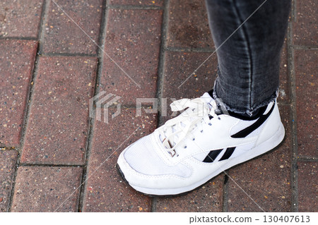 Stylish White Sneakers Lying on a Brick Pavement Surface Stylish White Sneakers Lying on a Brick Pavement Surface 130407613