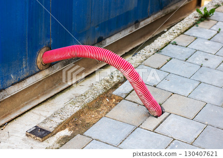 Vibrant Red Hose Emerging from Container on Paved Ground 130407621