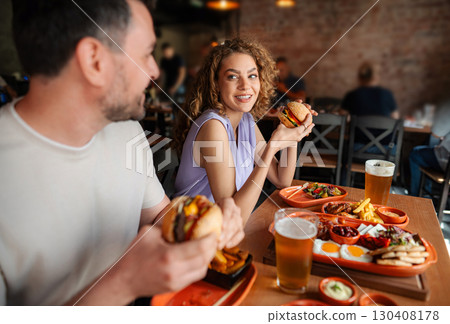 Couple eating burgers and drinking beer in restaurant 130408178