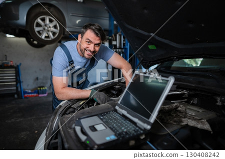 Car mechanic using a computer to diagnose a car engine problem Car mechanic using a computer to diagnose a car engine problem 130408242