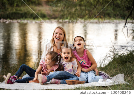 Mother and daughters laughing together during a picnic by the river 130408246