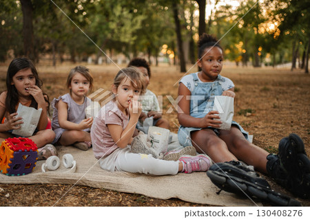 Children eating popcorn and watching a movie in the park Children eating popcorn and watching a movie in the park 130408276