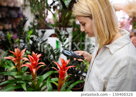 Woman botanist examining plants with magnifying glass in greenhouse 130408328