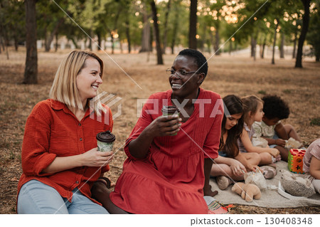 Smiling teachers enjoying coffee break in park while children playing Smiling teachers enjoying coffee break in park while children playing 130408348