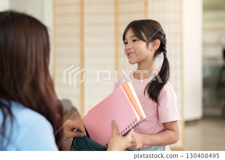 Child smiling while receiving school supplies from parent 130408495