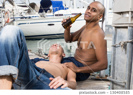 romantic couple of young men sitting and relaxing together on the pavement in the port romantic couple of young men sitting and relaxing together on the pavement in the port 130408585