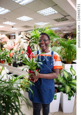 Young florist holding a guzmania plant, smiling and looking at camera 130408731