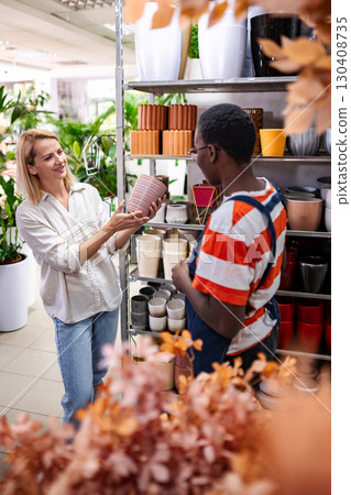 Shop assistant showing flowerpots to customer in garden center Shop assistant showing flowerpots to customer in garden center 130408735