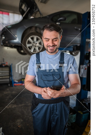 Happy mechanic using mobile phone in a car repair shop 130408752