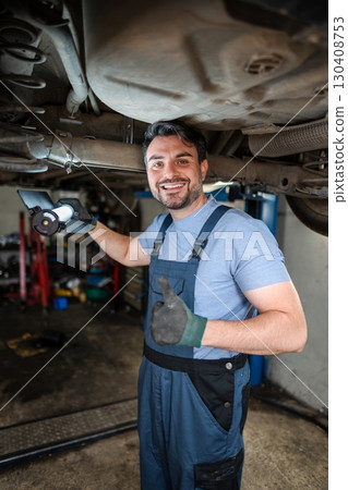 Smiling mechanic inspecting car chassis and showing thumbs up Smiling mechanic inspecting car chassis and showing thumbs up 130408753