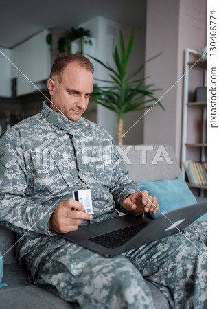 Soldier making online payment using laptop and credit card at home 130408774