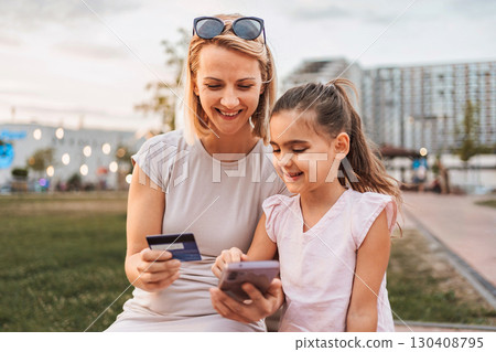 Mother and daughter making online payment using credit card and smartphone in city park Mother and daughter making online payment using credit card and smartphone in city park 130408795