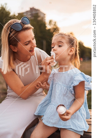 Mother cleaning her daughter's mouth with a napkin after eating ice cream in a park Mother cleaning her daughter's mouth with a napkin after eating ice cream in a park 130408802