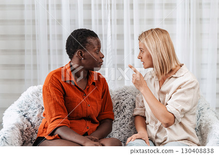 Two female friends arguing while sitting on a sofa at home Two female friends arguing while sitting on a sofa at home 130408838
