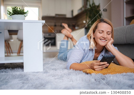 Woman relaxing on carpet using smartphone at home Woman relaxing on carpet using smartphone at home 130408850