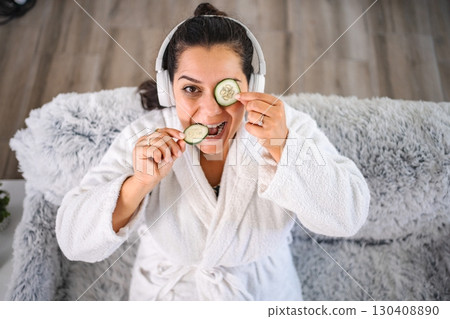 Woman wearing bathrobe is having fun during beauty treatment with cucumber slices 130408890