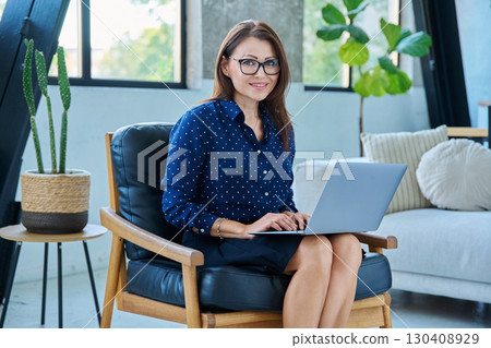 Portrait of middle aged woman with laptop sitting in chair 130408929