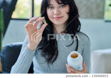 Close up of yellow Omega 3, fish oil capsule and bottle in hands of young woman 130408931