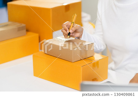 Woman start up small business owner writing address on cardboard box at workplace.small business entrepreneur SME or freelance asian woman working with box at home. Woman start up small business owner writing address on cardboard box at workplace.small business entrepreneur SME or freelance asian woman working with box at home. 130409861