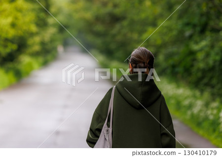 Woman walking on a serene path surrounded by lush greenery in a quiet moment of reflection Woman walking on a serene path surrounded by lush greenery in a quiet moment of reflection 130410179