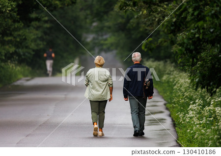 Elderly couple enjoys a leisurely stroll down a quiet, tree-lined pathway in the early morning light 130410186