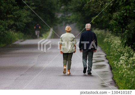 Couple walks leisurely along a serene, tree-lined road on a cloudy day 130410187