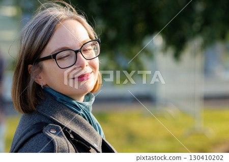 Woman enjoying a sunny day outdoors with eyes closed and a peaceful expression Woman enjoying a sunny day outdoors with eyes closed and a peaceful expression 130410202