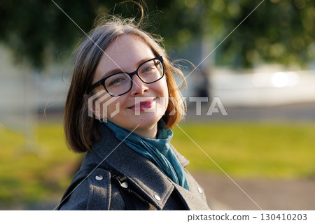 Smiling woman in glasses enjoys a sunny day while standing outdoors in a park with green trees Smiling woman in glasses enjoys a sunny day while standing outdoors in a park with green trees 130410203
