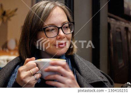 Woman enjoying coffee in a cozy cafe while wrapped in warm clothing during autumn afternoon Woman enjoying coffee in a cozy cafe while wrapped in warm clothing during autumn afternoon 130410231