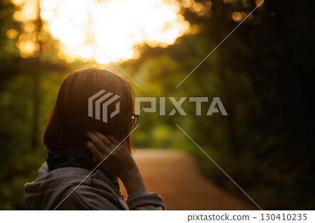 Woman enjoying a peaceful moment while walking on a quiet forest path at sunset 130410235