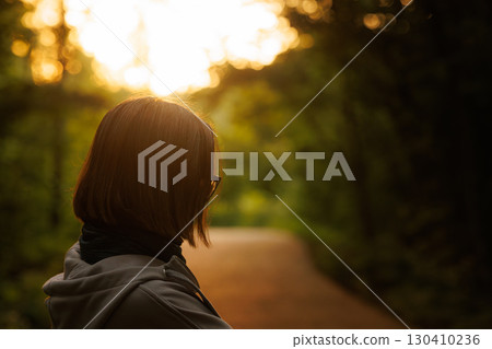 Individual enjoying a peaceful walk in the forest during sunset near a nature trail 130410236