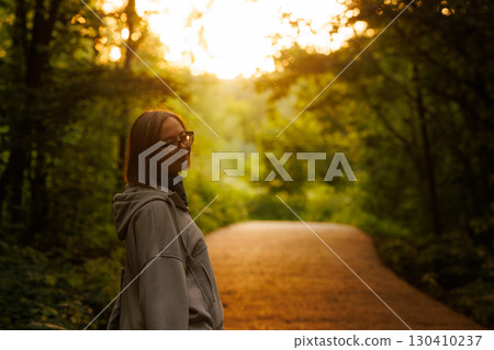Young woman enjoying a peaceful moment on a forest path at sunset 130410237